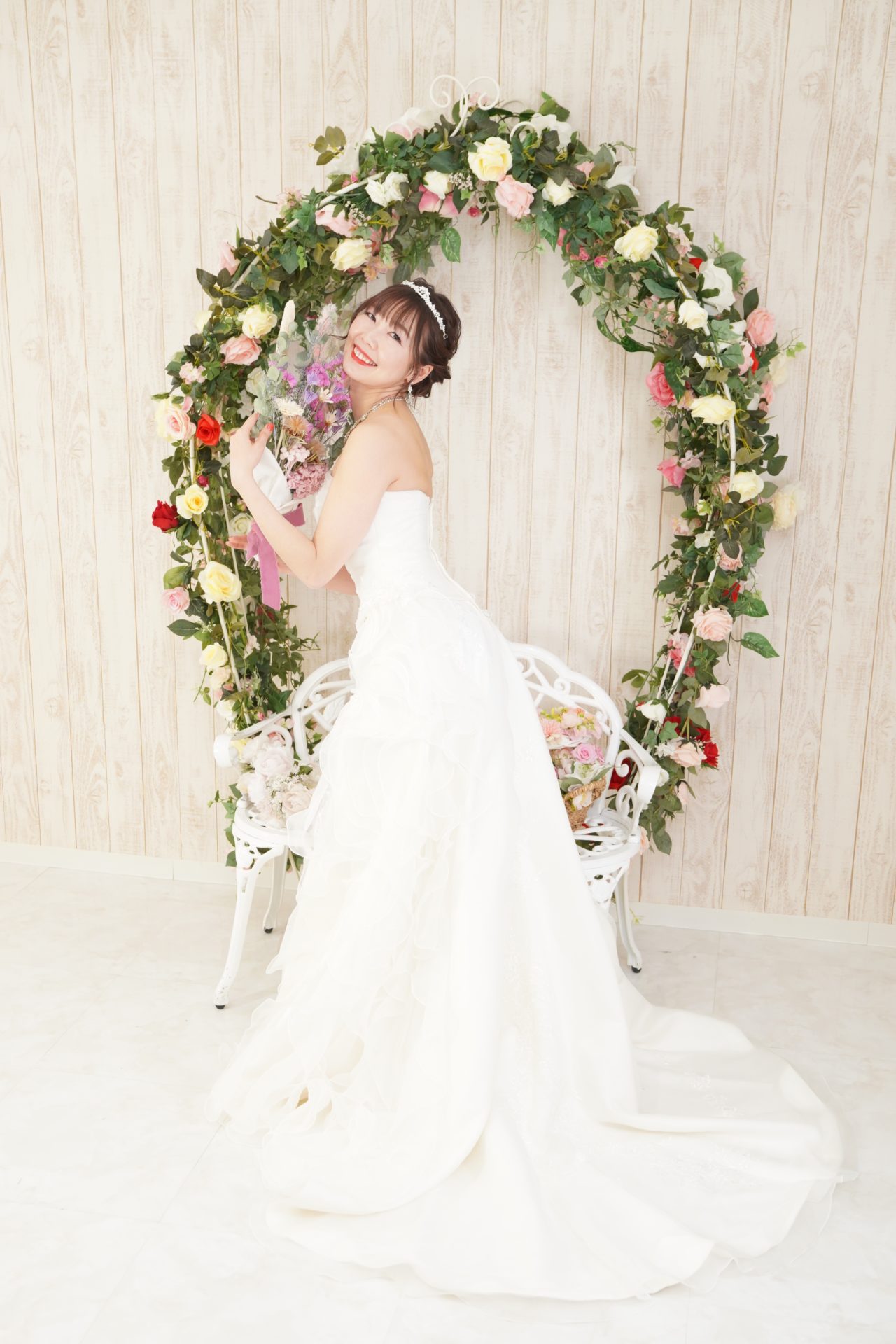 ウエディングドレスを着てブーケを持ち、お花のアーチの前でポーズを取る女性