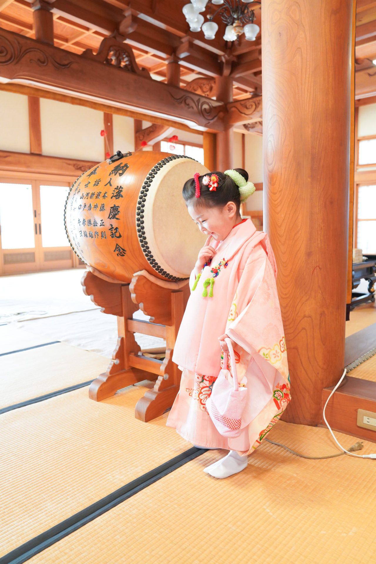 優しいピンクの着物を見に纏い、お寺の中で嬉しそうな表情の3歳の女の子の七五三