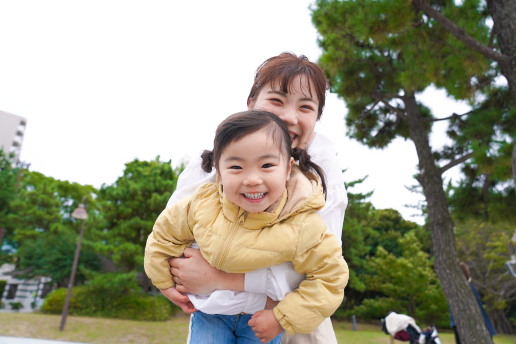 公園で、ママに後ろから抱きしめられ、嬉しそうな表情の女の子
