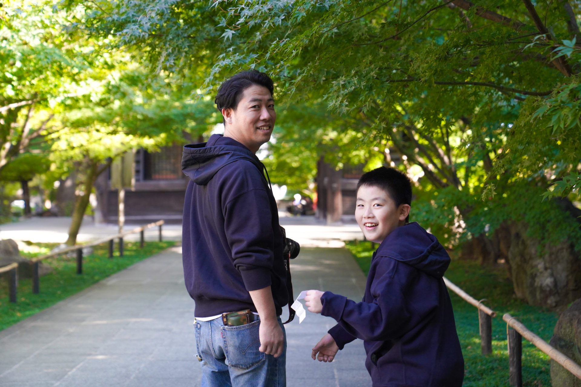 神社の境内を歩くペアルックのパパと男の子が、笑顔でこちらを振り返っています